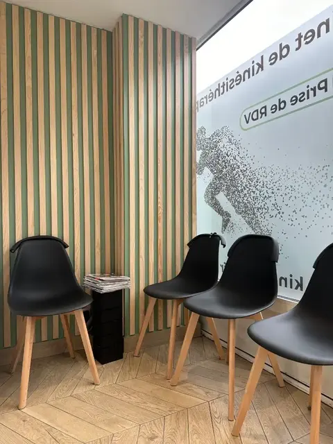 Salle d'attente du cabinet KineAthlea avec ses chaises noires et son mur boisé